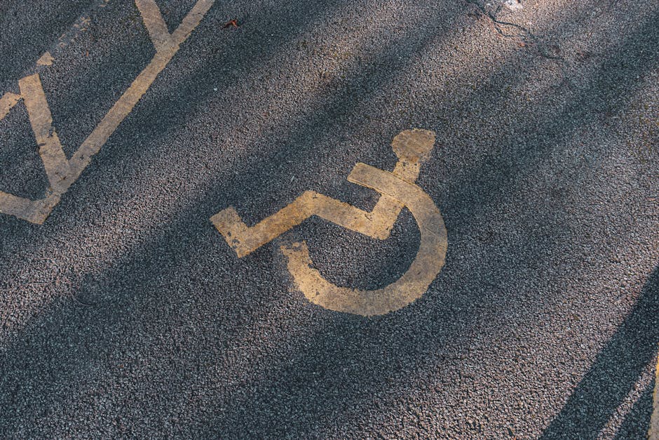 The image depicts an underground London Tube station platform with cream-colored tiled walls and a tiled floor featuring a speckled pattern. On the left side, there is a staircase with black metal railings leading up to an exit, accompanied by a yellow 'Way out' sign hanging from the ceiling. A blue sign with a wheelchair symbol indicates accessible routes. The platform edge is marked with a white line and a yellow tactile strip for safety, alongside a black rubber edging strip. A train with a red front is approaching or arriving at the platform in the background, partially obscured by the platform's curved design. Several large posters are mounted on the tiled wall, promoting various services and products, including a prominent poster for 'Moneybox.' The environment is lit with overhead fluorescent lighting, creating a well-illuminated space suitable for passenger transit. This scene aligns with the context of house removals and furniture transport, as part of a home relocation or moving process within London.